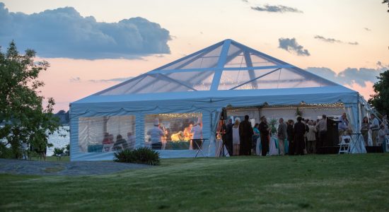 A large white outdoor banquet tent at dusk with guests mingling inside