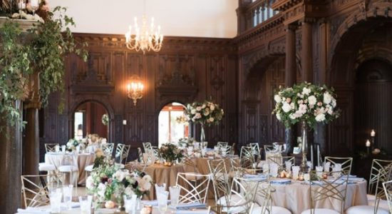 Branford House banquet hall with tables set for a formal dinner. Dramatic white and green floral arrangements in varying heights are displayed throughout.