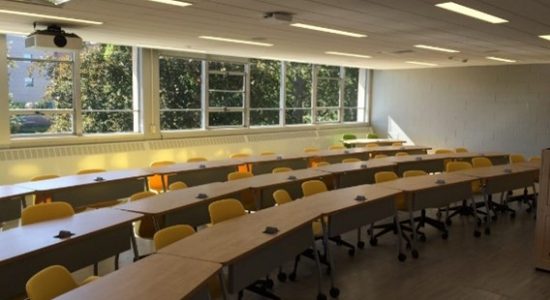 View of a Monteith 419 classroom. Three rows of long tables on risers with chairs face the front of the room.