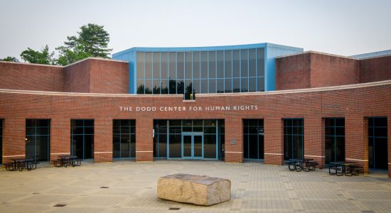 Exterior view of the main entrance to the Dodd Center for Human Rights building. A large stone sculpture of book is in the foreground of the patio leading to the entrance.