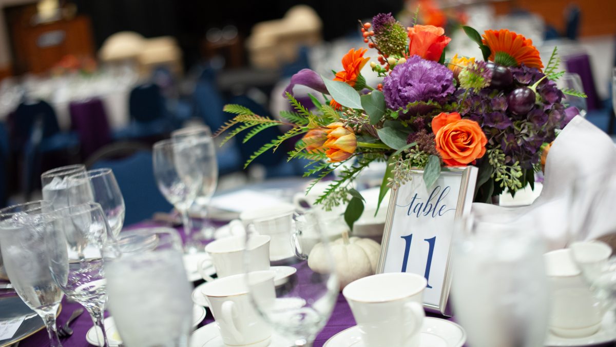 Banquet table with floral centerpiece, table number sign, coffee cups and water glasses