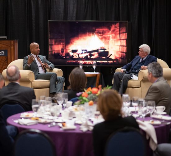 Dodd Prize recipient Bryan Stevenson chatting with Senator Christopher Dodd in front of a fireplace motif with a dinner audience in the foreground at a Dodd Prize event