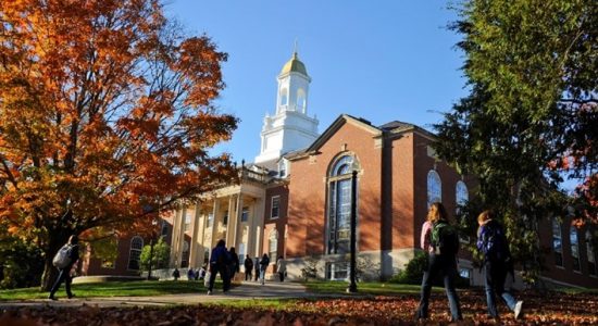 Exterior view of Wilbur Cross building in autumn. The gold dome of the building is visible and students are approaching the column-flanked main entrance.