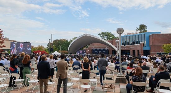 Group of people standing and listening to President Joe Biden speak on an outdoor stage outside the Dodd Center for Human Rights on the UConn campus.