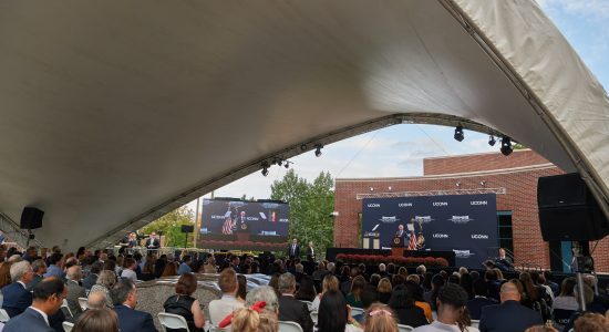 Crowd seated under a canopy outside the Dodd Center for Human Rights on the UConn campus listening to President Joe Biden speak at a podium.