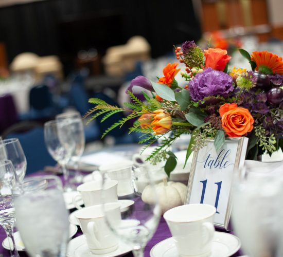 Close up view of a banquet table set for dinner service with a purple and orange floral centerpiece