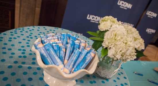 White Seashell shaped candy dish filled with blue wrapped candy bars next to a white hydrangea floral display. A navy blue UConn banner is visible in the background