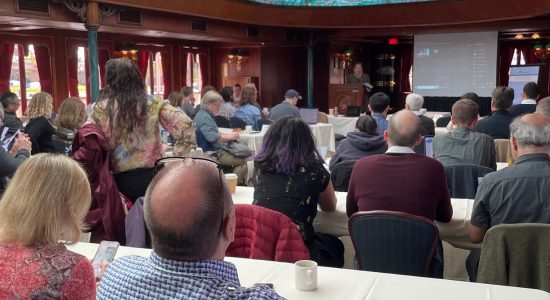 A audience seated at tables listening to a speaker during a NASA PACE 2023 conference event aboard a riverboat