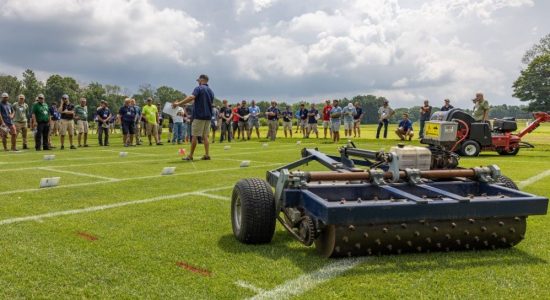 People viewing a landscaping equipment demonstration on an outdoor field during the 2022 UConn Turfgrass Field Conference