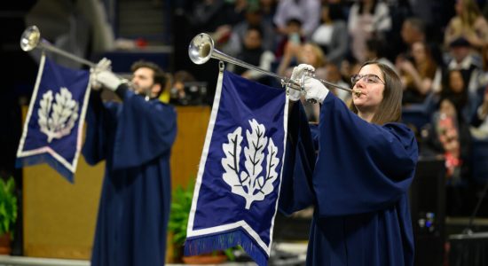 Individuals blowing ceremonial trumpets at a UConn commencement ceremony