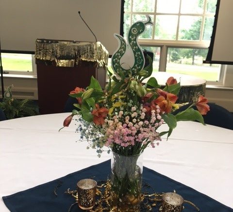 Floral centerpiece on a banquet table featuring a paper snake decoration and gold streamers with votives around the vase. There is a podium with gold tassels around it in the background