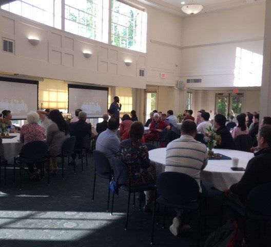 Conference attendees seated at banquet tables listening to a speaker at a podium