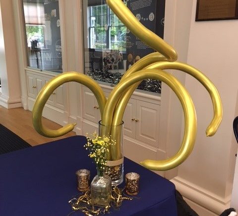 Curly gold balloon centerpiece display on a check-in table at the 2023 Dose Finding Conference