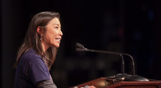 UConn Waterbury campus director Fumiko Hoeft smiling and speaking into microphones at a podium at the 2023 WISH Fest