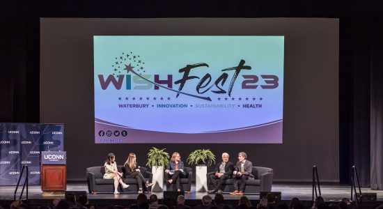 Panel of speakers seated on couches on stage at a 2023 WISH Fest event. In the background is a large screen with the WISH Fest logo on it.