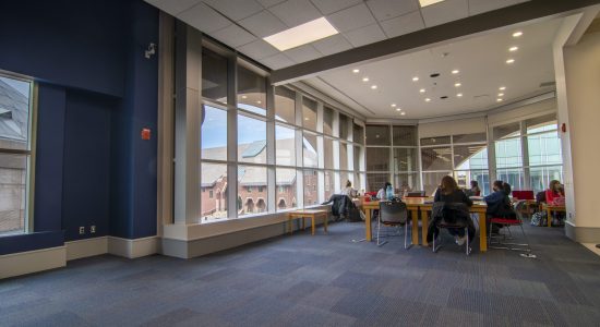 Students studying at tables in the UConn Bookstore Community Room. The room features large windows facing Gampel Pavilion.