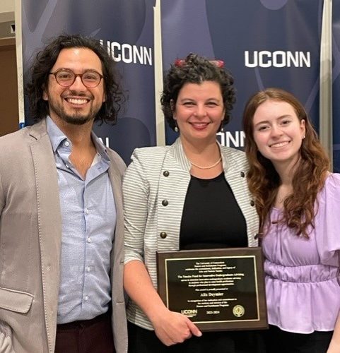 Three people smiling and holding an award plaque in front of a UConn banner at the 2023 UConn Honors event