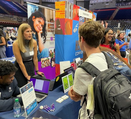 A student wearing a backpack chatting with a company representative at a career fair in Gampel Pavilion