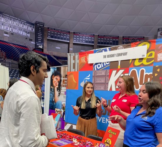 Student speaking to representatives at a Hershey Chocolate Company booth at a career fair in Gampel Pavilion