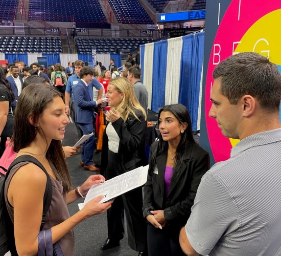 Professional representatives talking with a student at their booth at a career fair in Gampel Pavilion