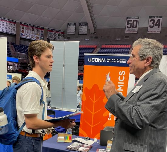 Student wearing a backpack chatting with a professional representative from a UConn department at a Career fair booth in Gampel Pavilion