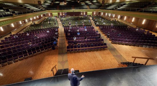 Jorgensen auditorium theater interior. A professor is on stage lecturing to widely scattered students in purple theater seats.