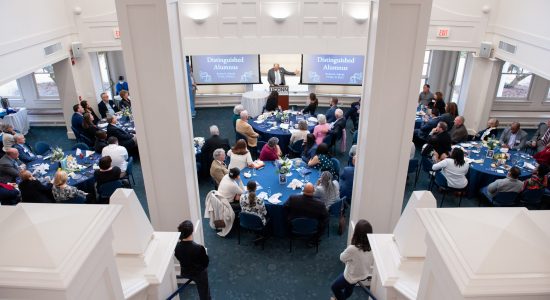 Overhead view of a banquet in the Alumni Center Banquet Hall with a speaker at a podium and screens on either side of the podium.