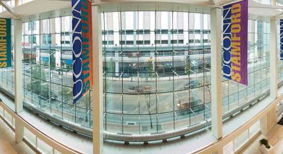 Interior view of a glass wall enclosed lobby of a Stamford campus building. A UConn Stamford banner is suspended from a column
