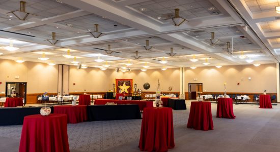 Rome Ballroom decorated for the 2023 Movies and Musicals themed Winter Holiday Celebration. Table of various sizes are draped in red and black tablecloths and there are gold accents throughout the room