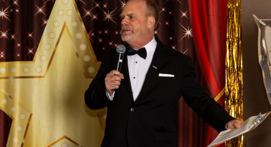 Leo Lachut on a Movies and Musicals themed stage acting as M.C. at the 2023 Winter Holiday Celebration