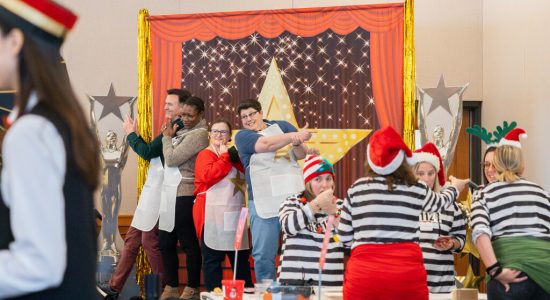 Gingerbread House contest team having their photo taken on a Movies and Musicals themed stage at the 2023 Winter Holiday Celebration event.