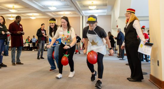 Gingerbread House contest team members competing in a challenge to race across the Rome Ballroom with a red balloon made to look like a tomato between their knees