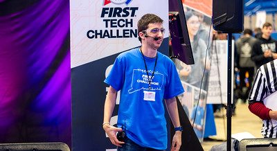 Individual wearing a headset with microphone smiling and observing the 2024 FTC Robotics Tournament at UConn.