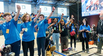 Robotics student team members wearing blue tee shirts, raising their fists in celebration at the 2024 FTC Robotics Tournaments at UConn.