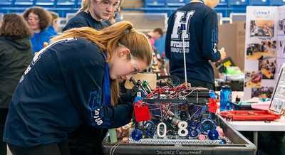 A robotics student bending over a cart, working on their robot at the 2024 FTC Robotics Tournament at UConn.