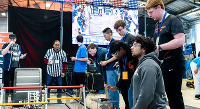 Two teams of robotics students compete at the 2024 FTC Robotics Tournament at UConn. In the background a referee and announcer with a microphone look on.