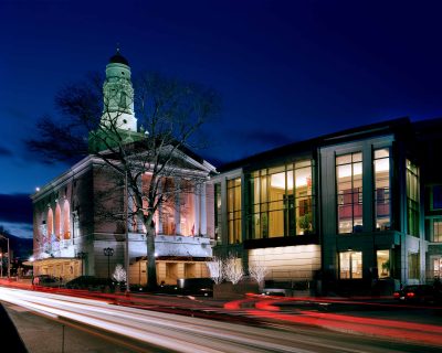 The Bushnell theater building at night with lights glowing and blurred cars driving by.